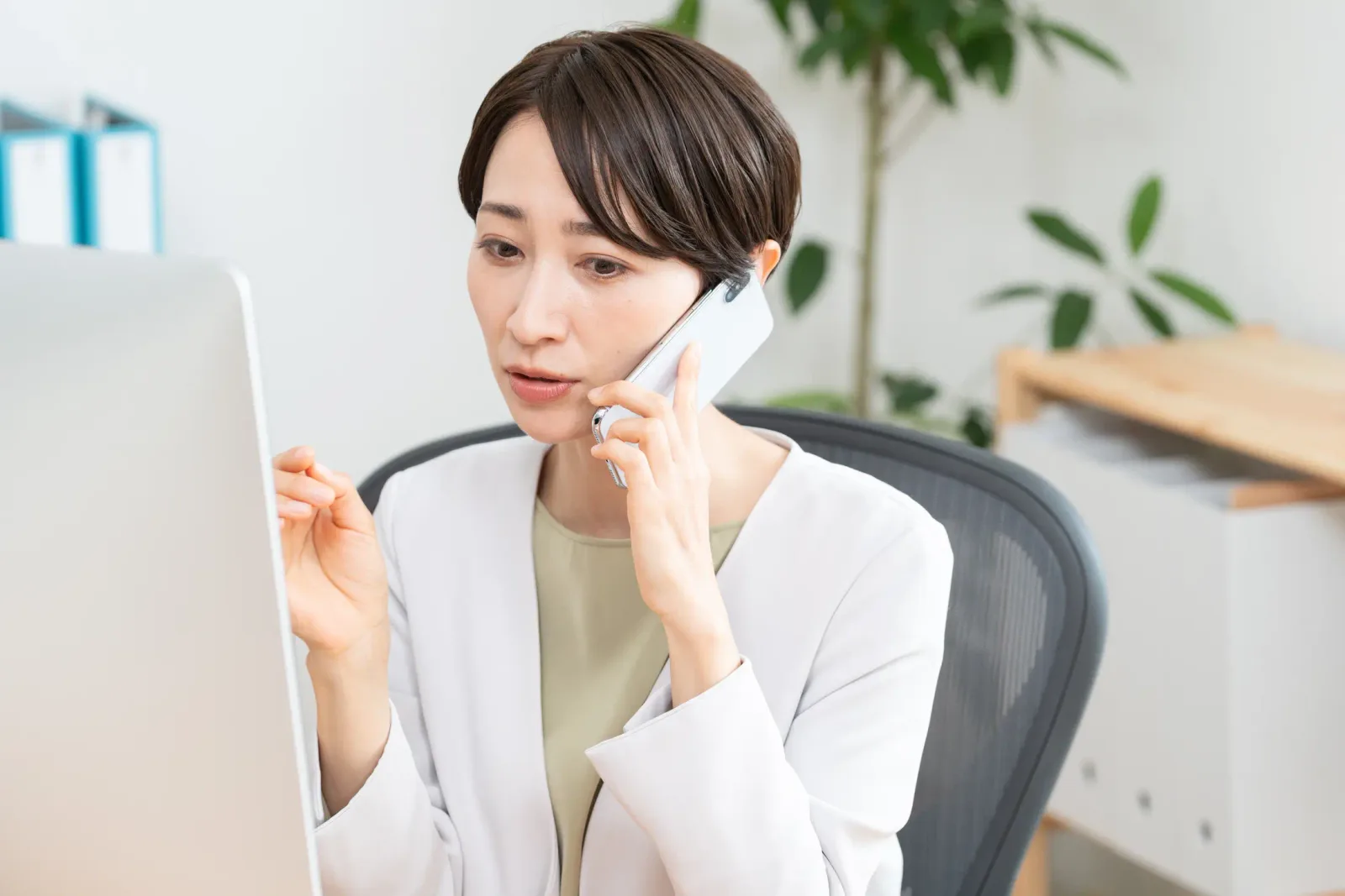 A woman at her desk taking a call on her mobile while working at the computer